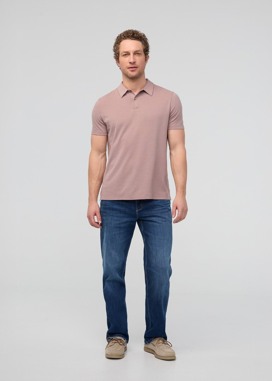 Man wearing a pink polo shirt and blue jeans on a light gray background