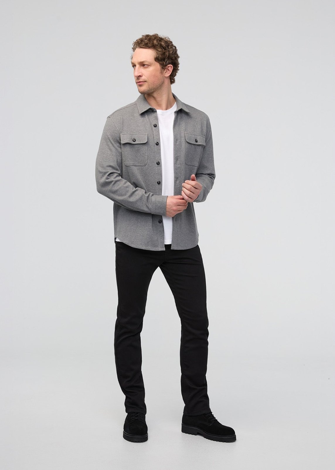 Man wearing a gray jacket over a white shirt with black pants on a light gray background