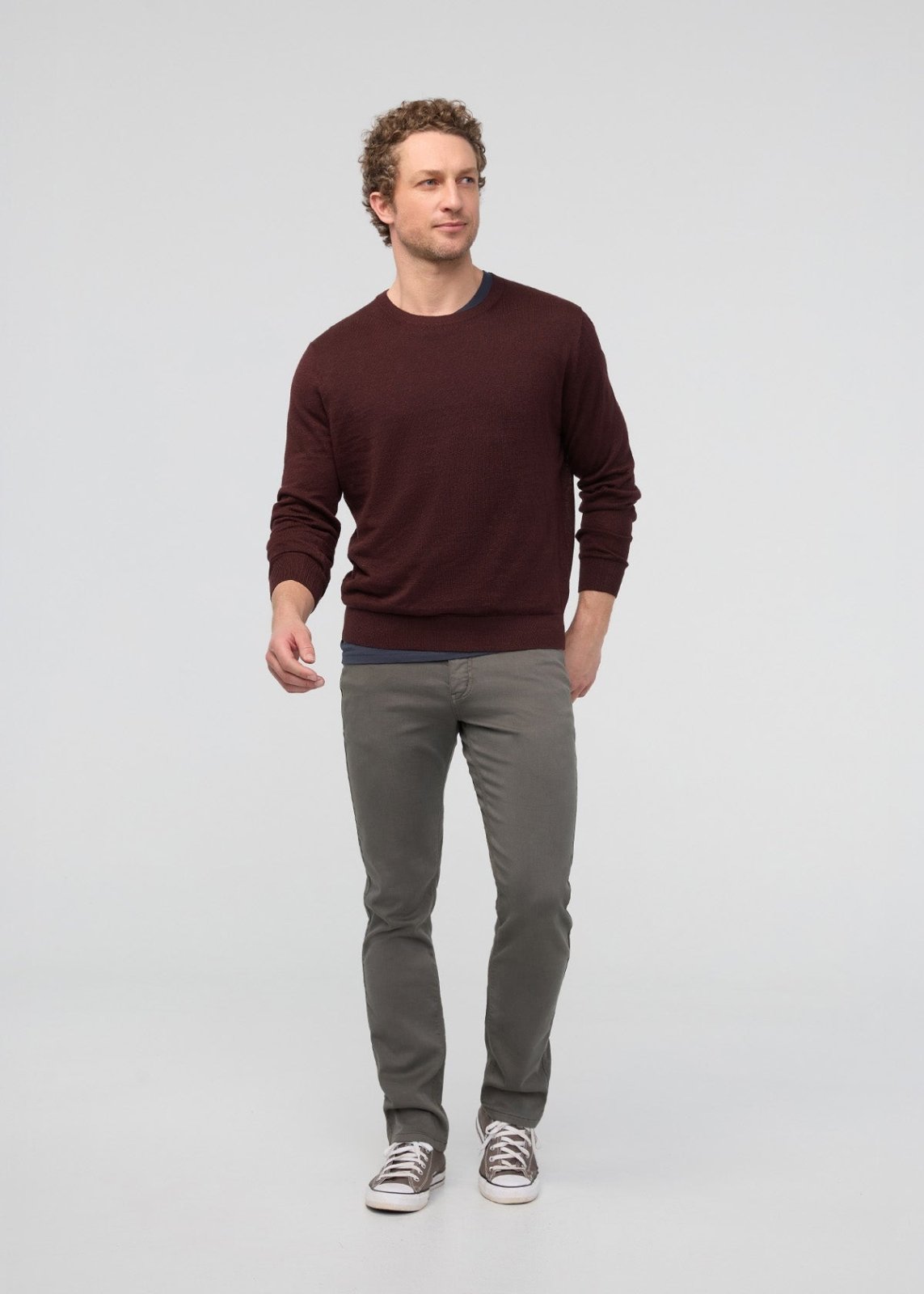 Man wearing a maroon sweater and gray pants on a light gray background
