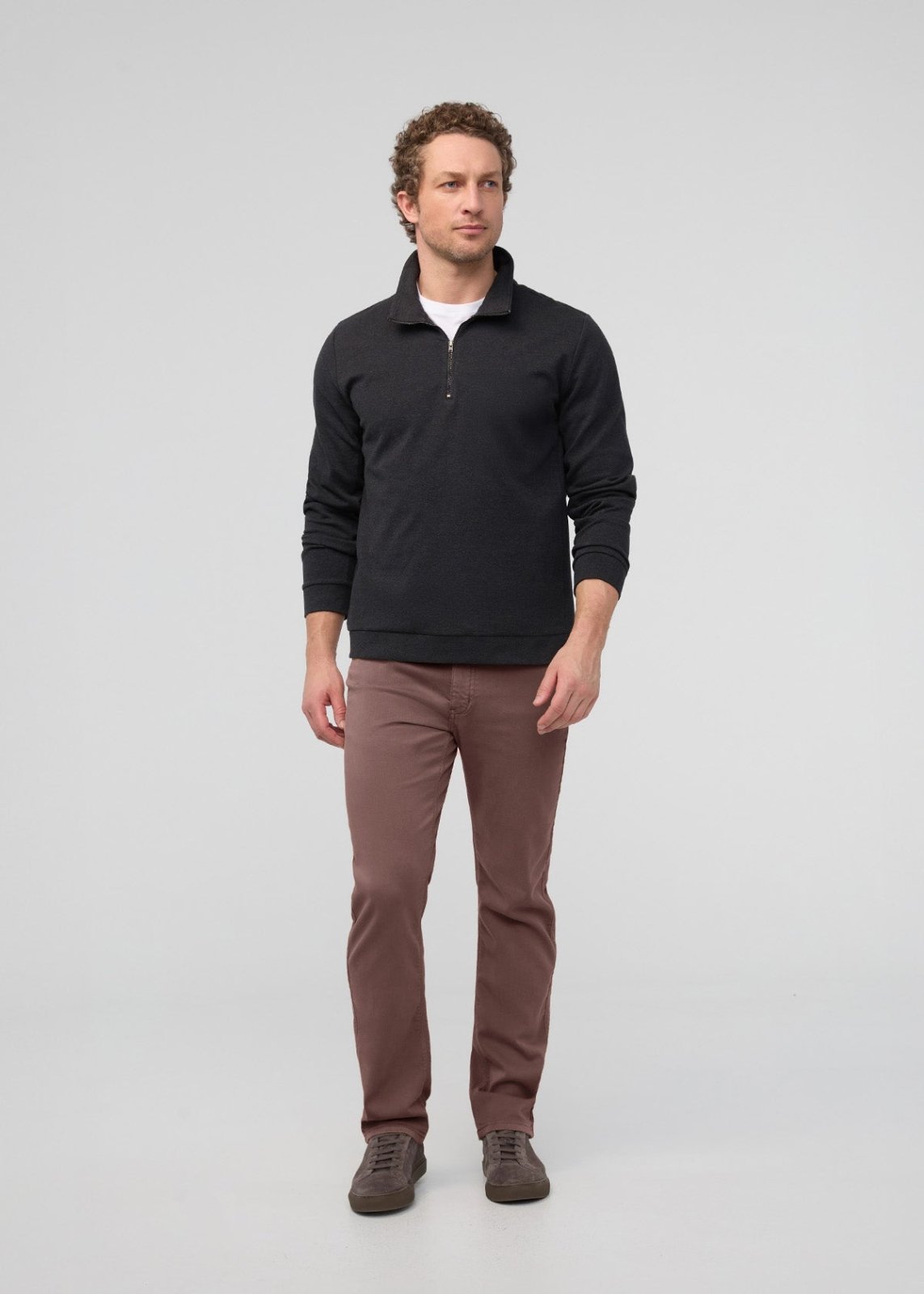 Man wearing black quarter-zip sweatshirt, brown pants, and gray sneakers.