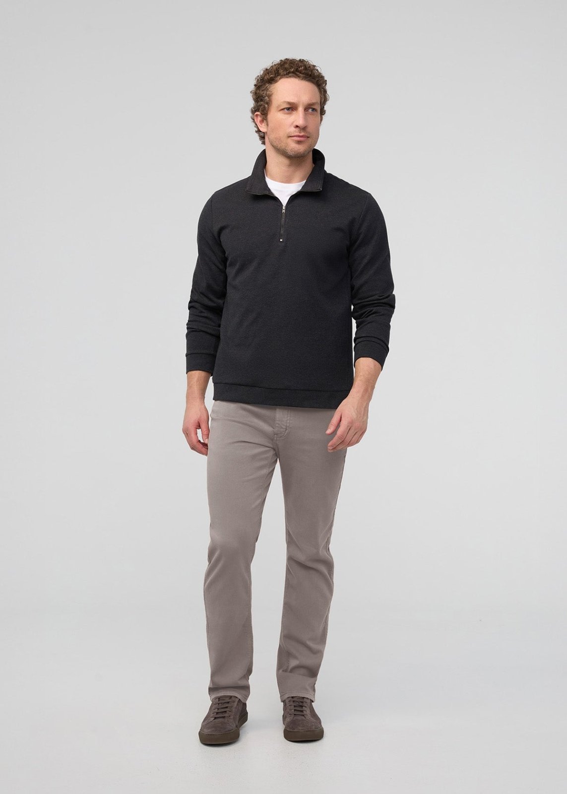 Man wearing black quarter-zip pullover with white undershirt and stone-colored straight-leg pants.