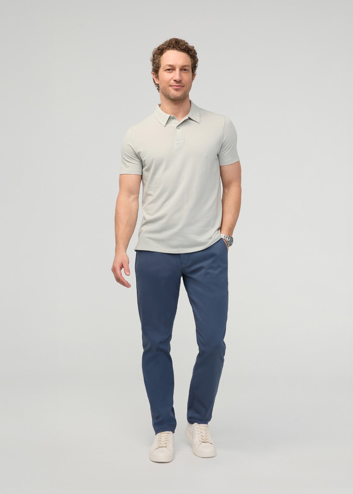 Man wearing light gray polo shirt and dark blue tapered trousers with cream sneakers.