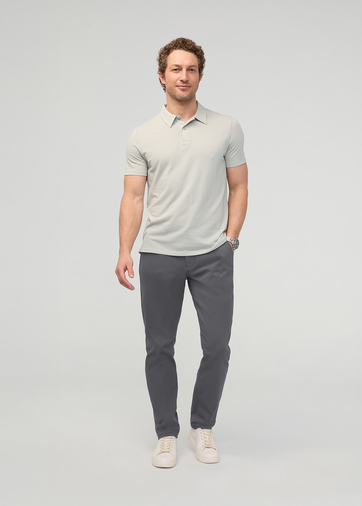 Man wearing light gray polo shirt and dark gray tapered trousers with white sneakers.