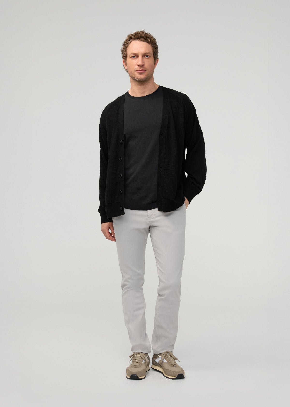 Man wearing light gray straight-leg chinos with black cardigan and black t-shirt.
