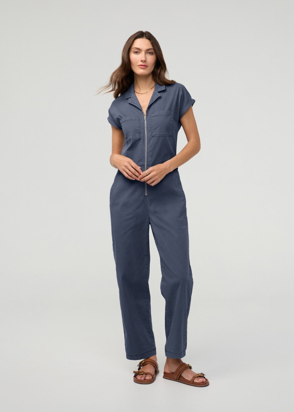 Blue boiler suit with short sleeves, collared neckline, and front zip closure worn by a woman with brown sandals.