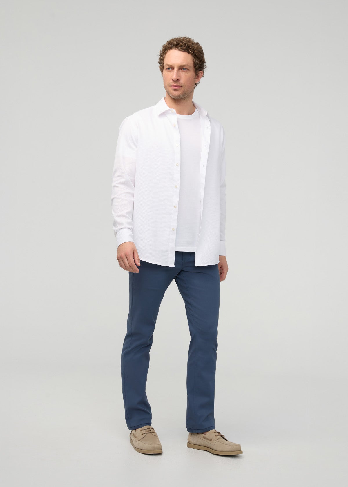 Man wearing dark blue slim straight trousers with white button-up shirt and tan loafers.