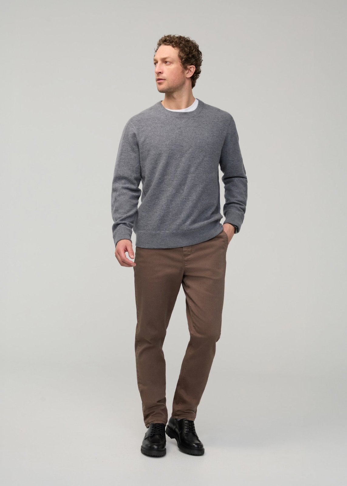 Man wearing gray crew neck sweater and tan pull-on pants with black boots.