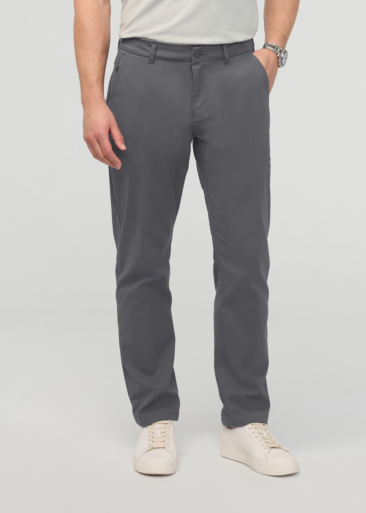 Man wearing dark gray relaxed taper trousers with a cream shirt and white sneakers.