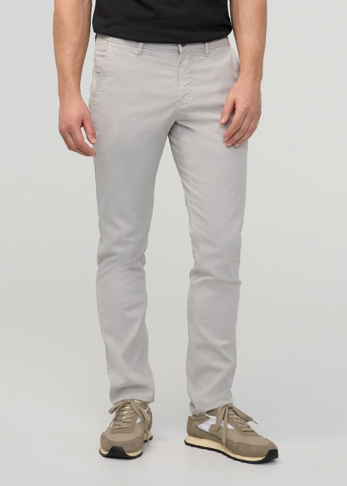 Man wearing light gray straight-leg chino pants with a black shirt and beige sneakers.