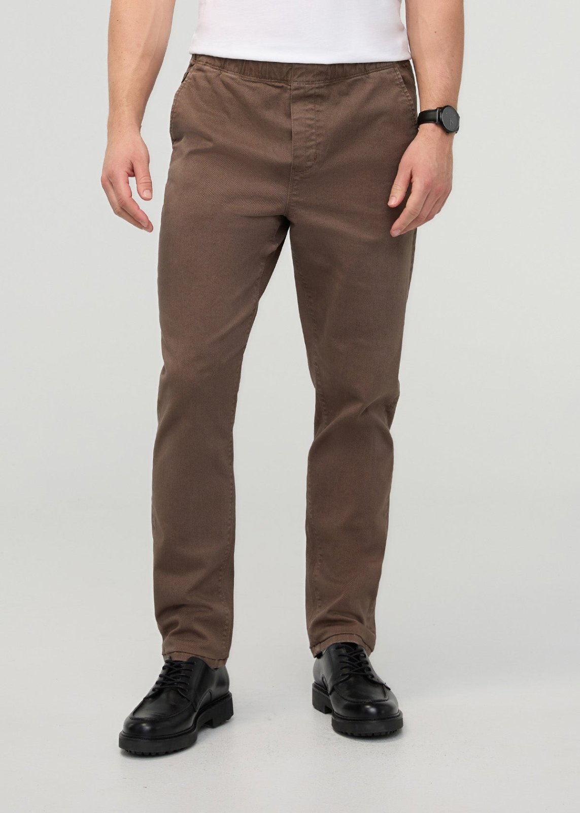 Man wearing brown relaxed pull-on pants with elastic waistband and black lace-up shoes.