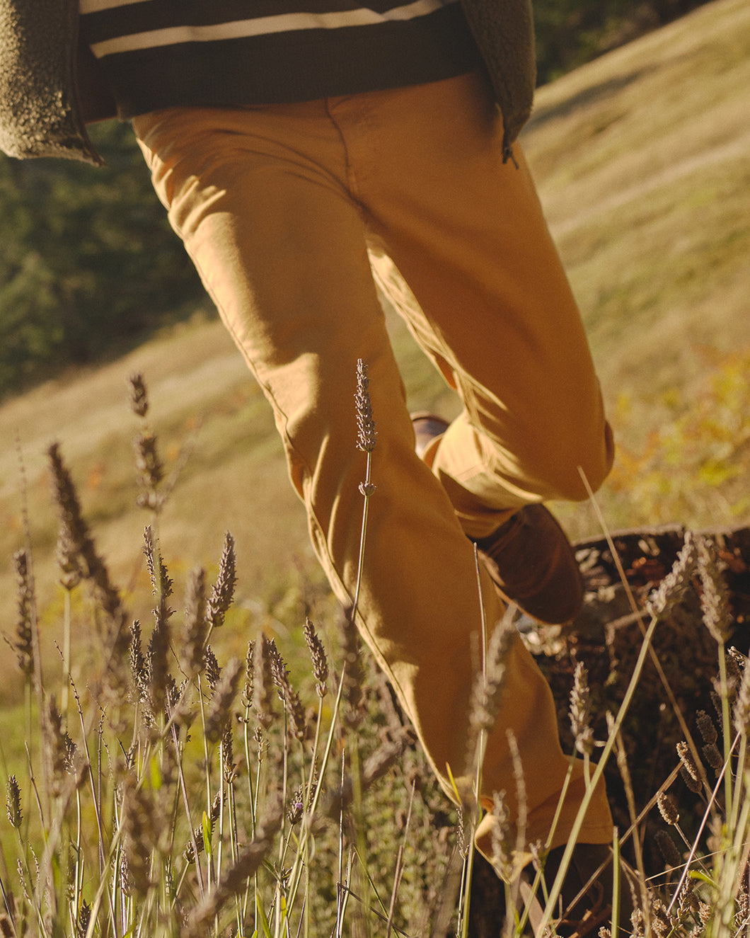 Close up of a person from the waist down wearing yellow pants running through a field. 