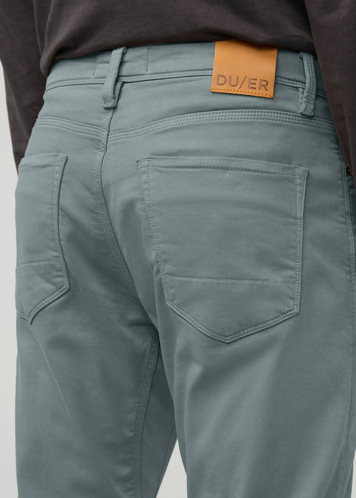 Blue spruce relaxed taper pants with orange DU/ER label on waistband, shown from back view with visible pocket stitching.