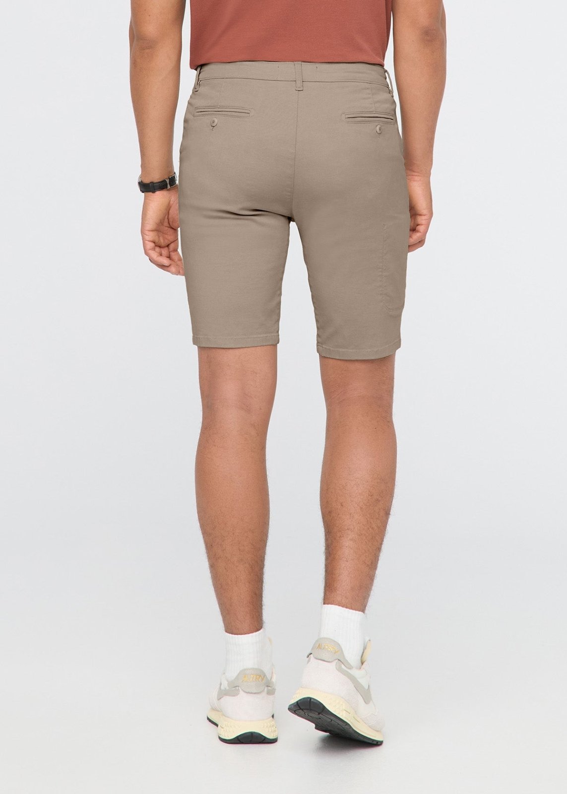 Sandstone shorts with flat front pockets and button closure, shown from behind on model wearing white socks and sneakers.