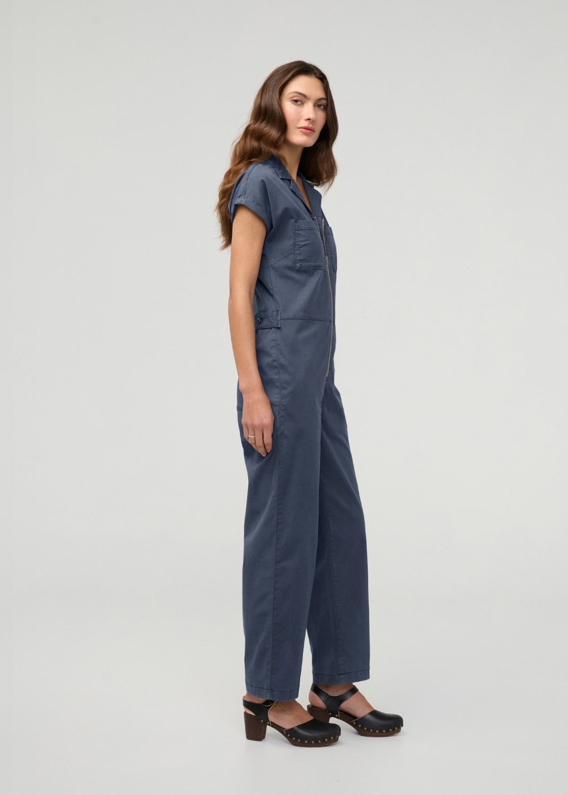 Woman wearing a blue boiler suit with short sleeves, front zip closure, and chest pockets.