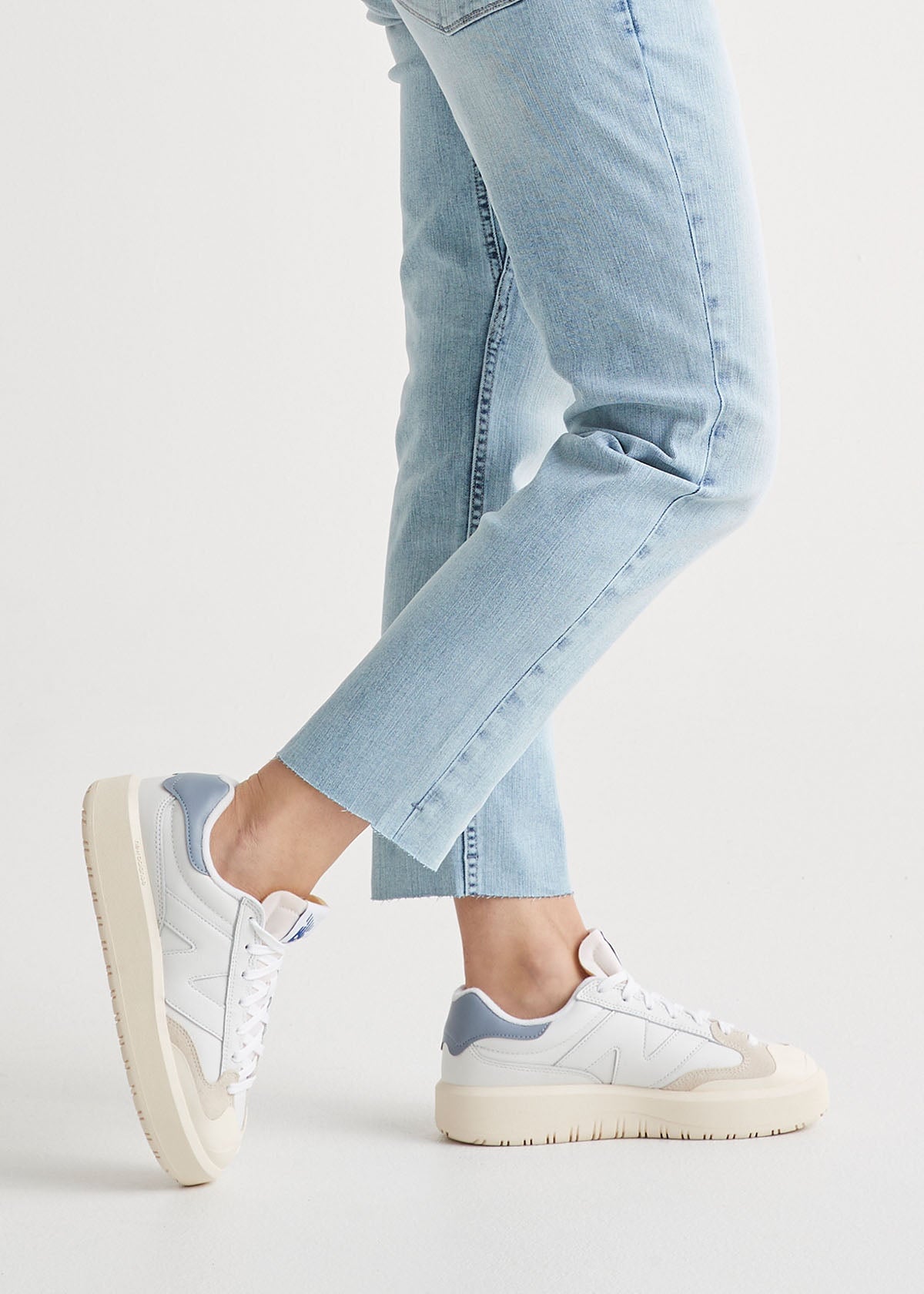 Light blue denim girlfriend jeans with raw hem worn with white and gray sneakers.