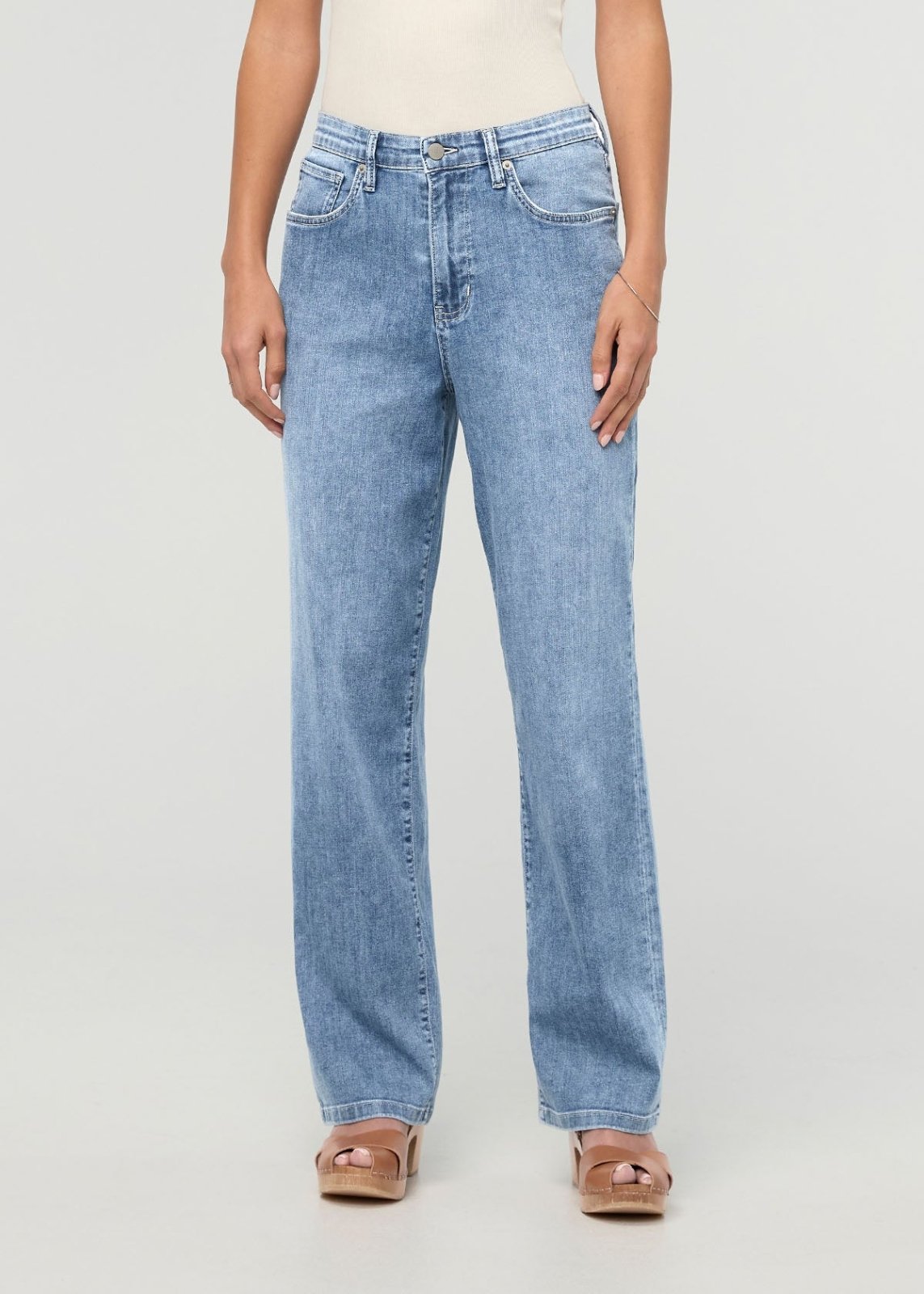 Light blue high-rise straight denim jeans with five-pocket styling on a model wearing a cream top and tan platform sandals.