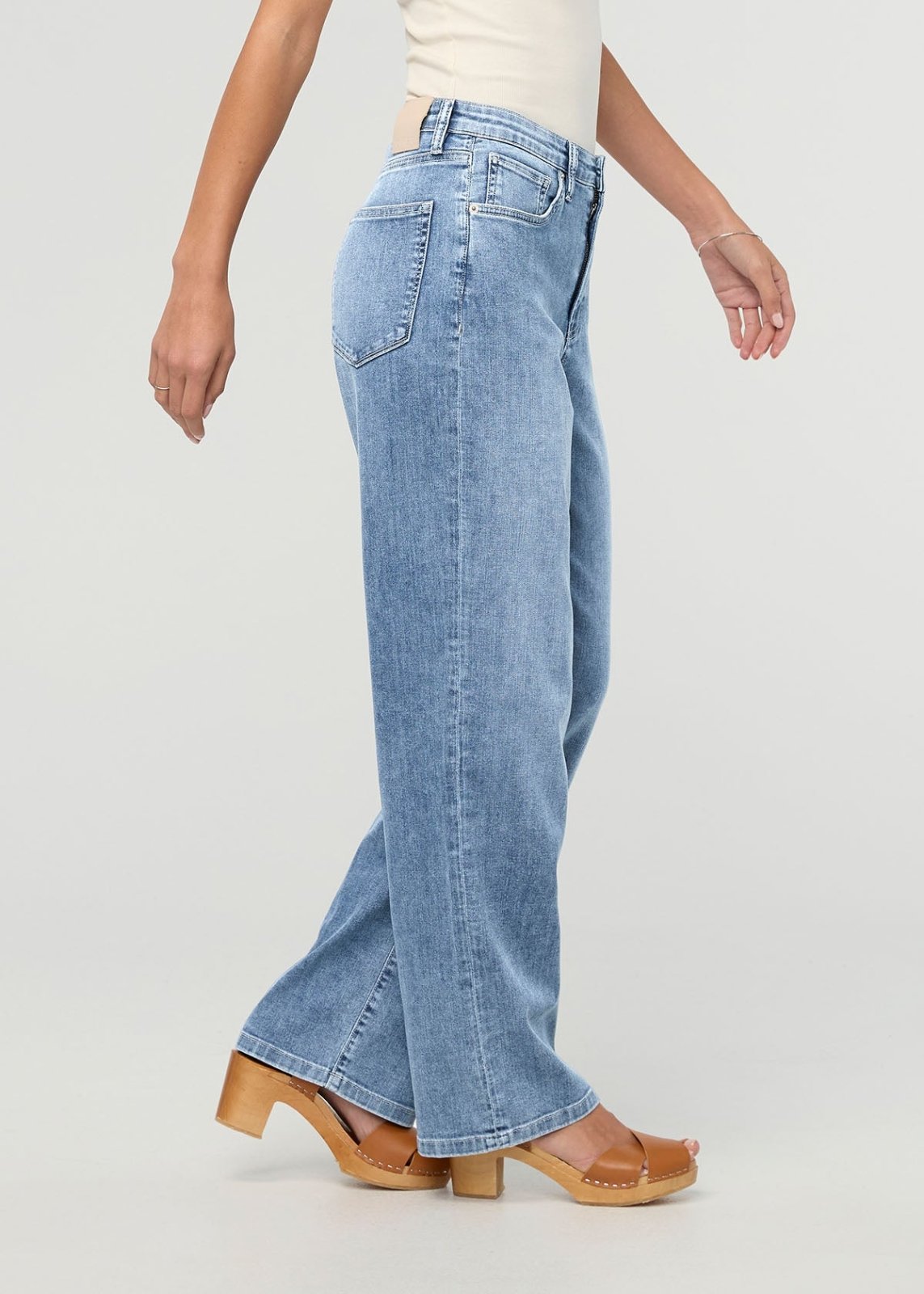 Light stone wash high-rise straight leg denim jeans on model wearing cream top and wooden platform sandals.